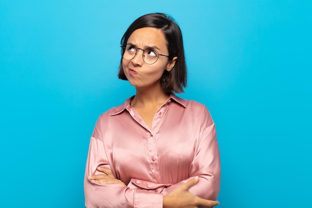 Jeune femme hispanique avec une expression inquiète, confuse et désemparée, levant les yeux pour copier l'espace, doutant