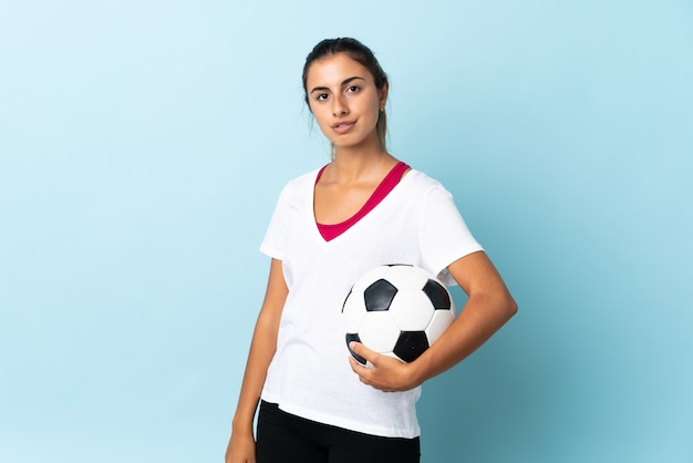 Jeune femme hispanique sur fond bleu isolé avec ballon de foot