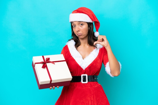 Jeune femme hispanique habillée en maman noel tenant un cadeau isolé sur fond bleu fier et satisfait de soi