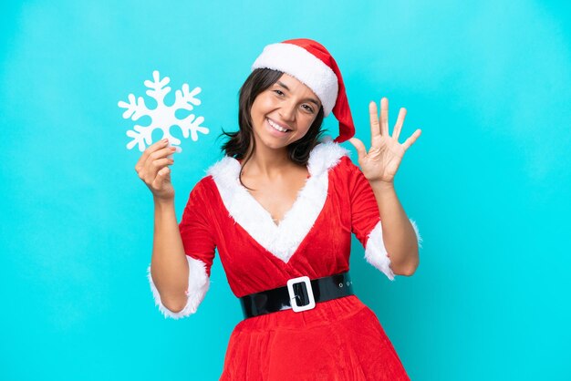 Photo jeune femme hispanique habillée en maman noel tenant un flocon de neige isolé sur fond bleu en comptant cinq avec les doigts