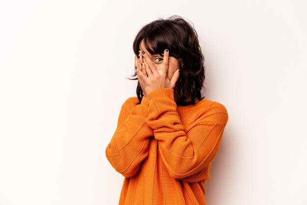 Jeune femme hispanique isolée sur fond blanc clignote à travers les doigts effrayée et nerveuse