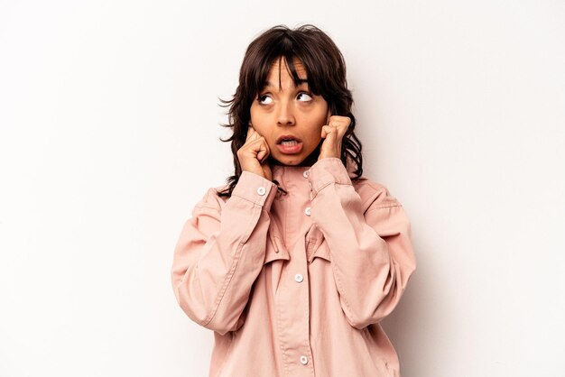 Jeune femme hispanique isolée sur fond blanc couvrant les oreilles avec les doigts stressés et désespérés par une ambiance bruyante