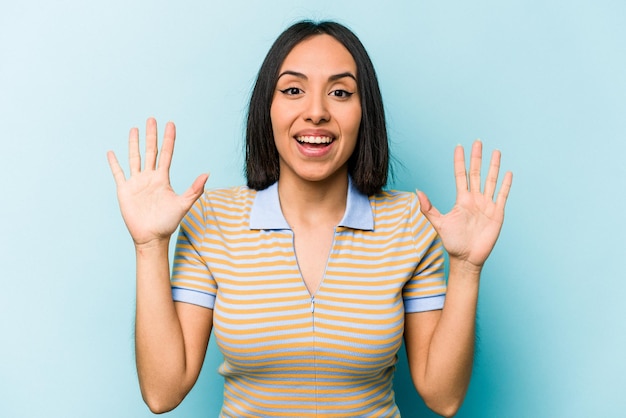 Jeune femme hispanique isolée sur fond bleu recevant une agréable surprise excitée et levant les mains