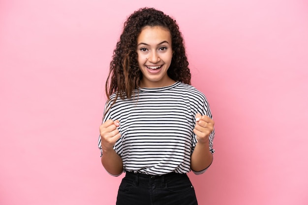 Jeune femme hispanique isolée sur fond rose célébrant une victoire en position de gagnant