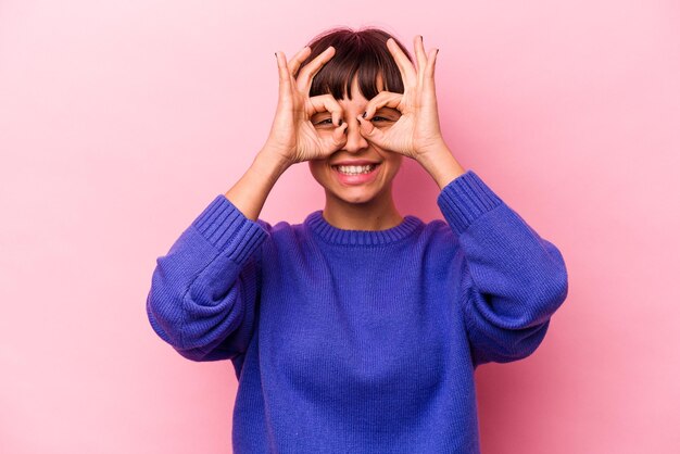 Jeune femme hispanique isolée sur fond rose excitée en gardant le geste ok sur les yeux