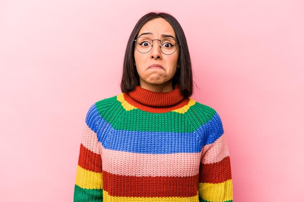 Jeune femme hispanique isolée sur fond rose hausse les épaules et ouvre les yeux confus