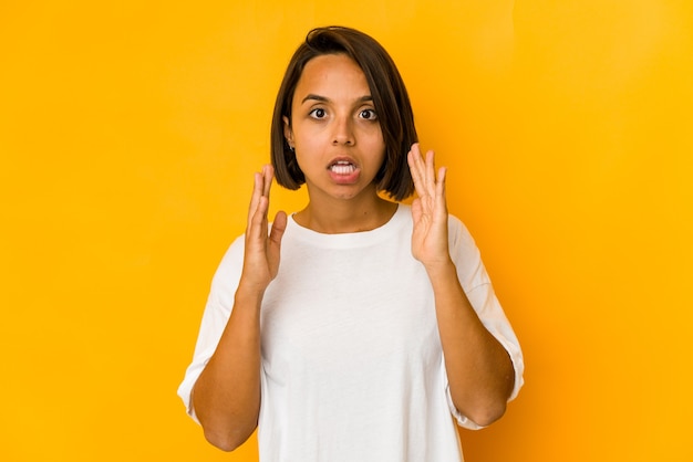 Jeune femme hispanique isolée sur jaune recevant une agréable surprise, excitée et levant les mains.