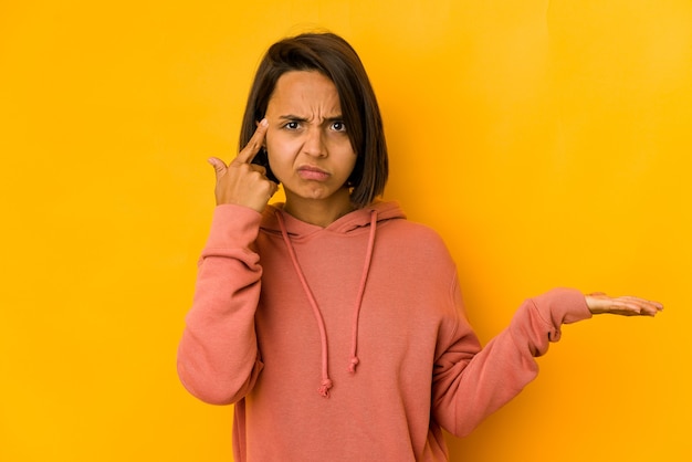 Jeune femme hispanique isolée sur tenant jaune et montrant un produit sous la main.