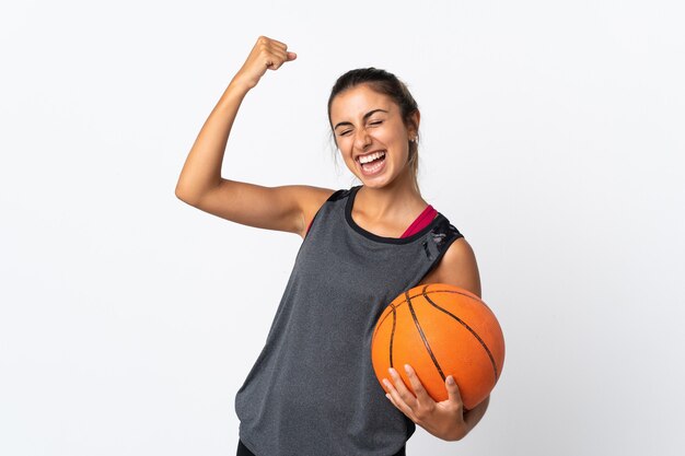 Jeune femme hispanique jouant au basket-ball sur un mur blanc isolé célébrant une victoire