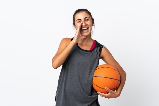 Jeune femme hispanique jouant au basket-ball sur un mur blanc isolé en criant avec la bouche grande ouverte