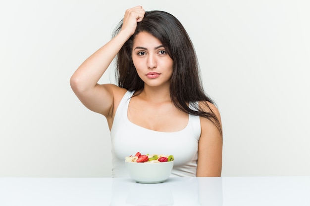 Jeune femme hispanique mangeant un bol de fruits en état de choc, elle s'est souvenue d'une réunion importante.