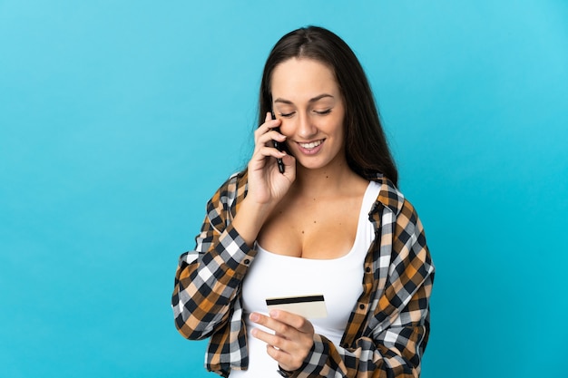 Jeune femme hispanique sur mur bleu isolé l'achat avec le mobile avec une carte de crédit