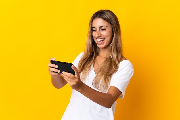 Jeune femme hispanique sur mur jaune isolé jouant avec le téléphone mobile