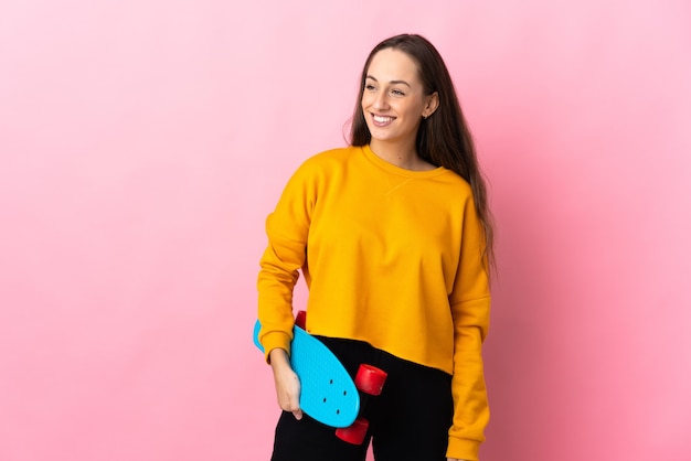 Jeune femme hispanique sur mur rose isolé avec un patin