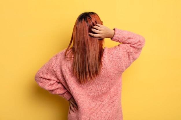 Jeune femme hispanique pensant ou doutant, se grattant la tête, se sentant perplexe et confus, vue arrière ou arrière