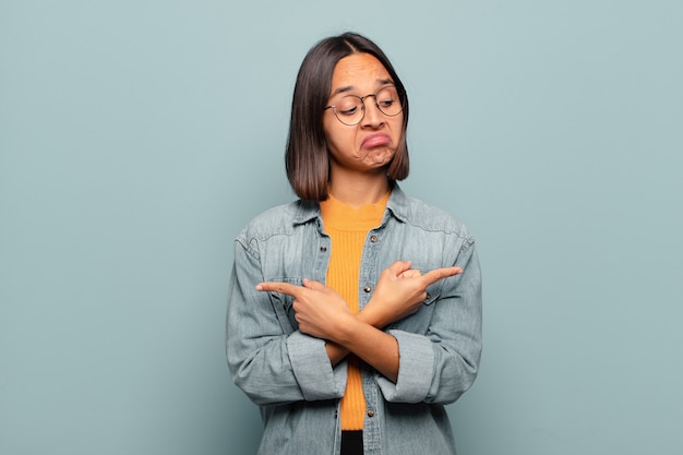 Jeune femme hispanique à la perplexité et à la confusion, l'insécurité et pointant dans des directions opposées avec des doutes