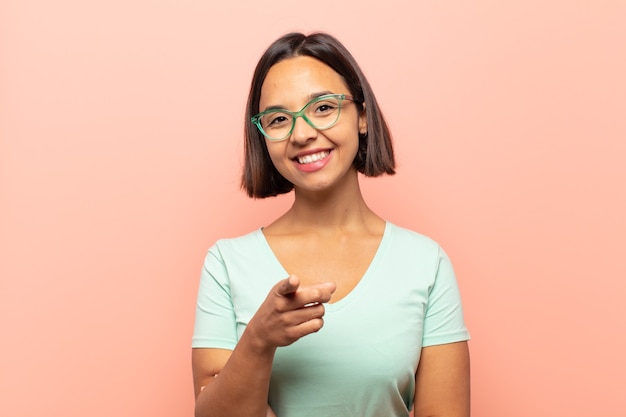 Jeune femme hispanique pointant vers l'avant avec un sourire satisfait, confiant et amical, vous choisissant