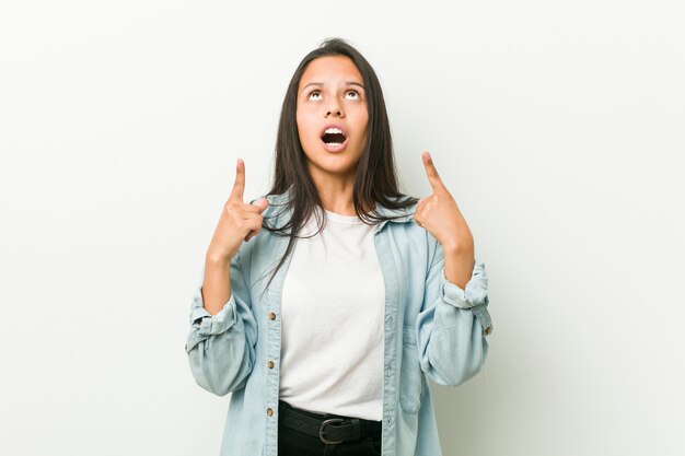 Jeune femme hispanique pointant vers le haut avec la bouche ouverte.