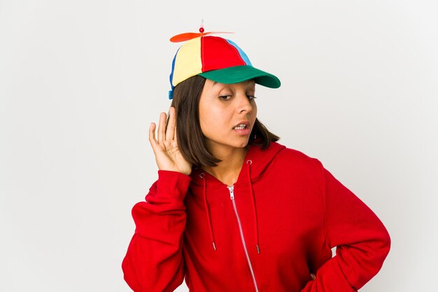 Jeune femme hispanique portant une casquette avec hélice isolée essayant d'écouter un commérage.