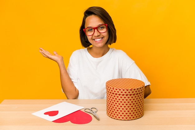 Jeune femme hispanique préparant un cadeau de la Saint-Valentin isolé montrant un espace de copie sur une paume et tenant une autre main sur la taille.