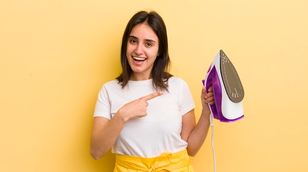 Jeune femme hispanique qui a l'air excitée et surprise en montrant le concept de fer à repasser