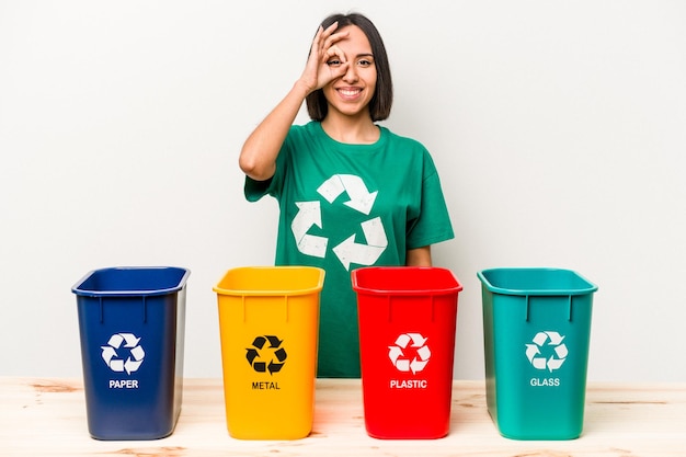 Jeune femme hispanique recyclage isolé sur fond blanc excité en gardant le geste ok sur les yeux