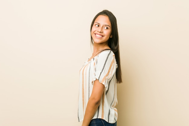 Jeune femme hispanique regarde de côté en souriant, joyeuse et agréable.