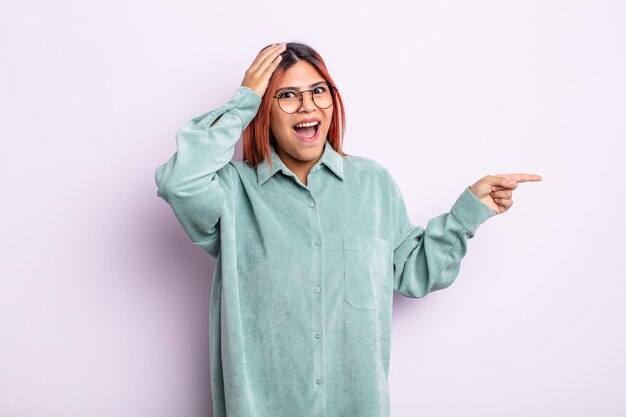 Jeune femme hispanique en riant, l'air heureux, positif et surpris de réaliser une excellente idée pointant vers l'espace de copie latéral