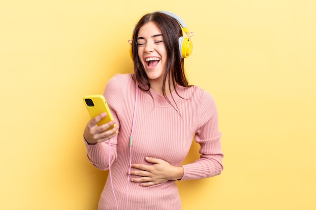 Jeune femme hispanique riant aux éclats d'une blague hilarante. casque et concept de téléphone