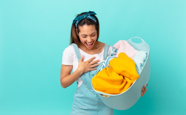 Jeune femme hispanique riant aux éclats d'une blague hilarante et lavant les vêtements