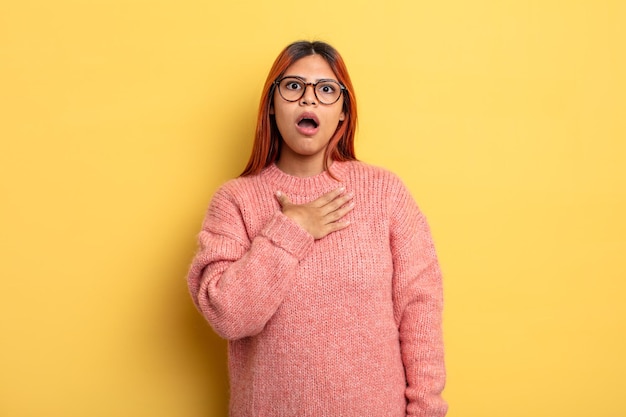 jeune femme hispanique se sentant choquée, étonnée et surprise, la main sur la poitrine et la bouche ouverte, disant qui, moi ?