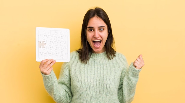 Jeune femme hispanique se sentant choquée en riant et en célébrant le concept de puzzle de succès