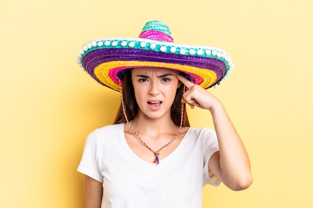 Jeune femme hispanique se sentant confuse et perplexe, montrant que vous êtes fou. concept de chapeau mexicain