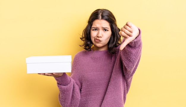 Jeune femme hispanique se sentant croisée, montrant les pouces vers le bas. concept de boîte vide