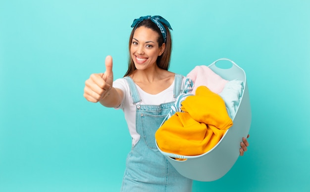 Jeune femme hispanique se sentant fière, souriante positivement avec les pouces vers le haut et lavant les vêtements