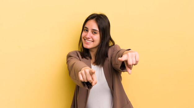 Jeune femme hispanique se sentant heureuse et confiante pointant vers la caméra avec les deux mains et riant en vous choisissant