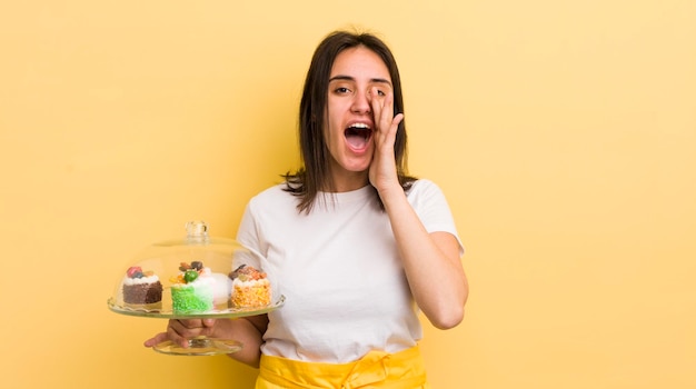 Jeune femme hispanique se sentant heureuse de donner un grand cri avec les mains à côté de la bouche concept de gâteaux faits maison