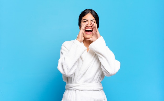 Jeune femme hispanique se sentant heureuse, excitée et positive, donnant un grand cri avec les mains à côté de la bouche, appelant. concept de peignoir