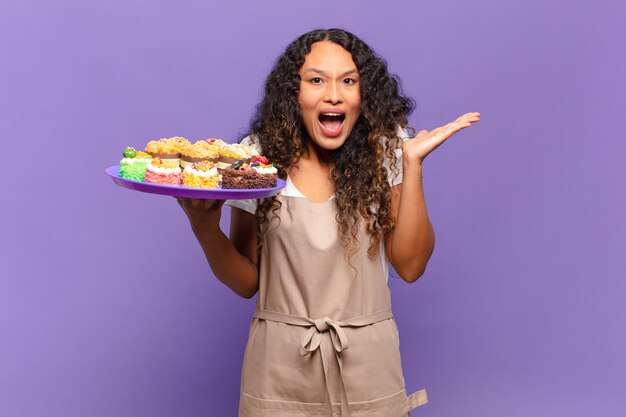 jeune femme hispanique se sentant heureuse, excitée, surprise ou choquée, souriante et étonnée de quelque chose d'incroyable. concept de gâteaux de cuisson