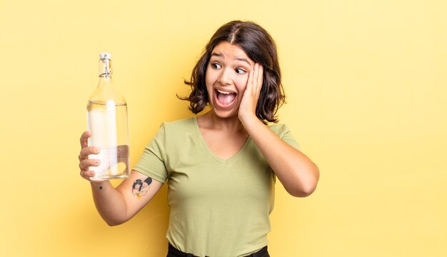 Jeune femme hispanique se sentant heureuse, excitée et surprise. concept de bouteille d'eau