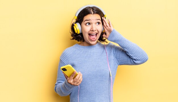 Jeune femme hispanique se sentant heureuse, excitée et surprise. concept de casque et smartphone