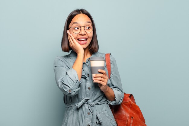 jeune femme hispanique se sentant heureuse, excitée et surprise, regardant de côté avec les deux mains sur le visage