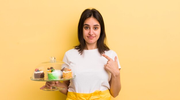 Jeune femme hispanique se sentant heureuse et pointant vers soi avec un concept de gâteaux faits maison excité