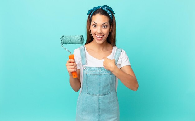 Jeune femme hispanique se sentant heureuse et pointant vers soi avec un excité et peignant un mur