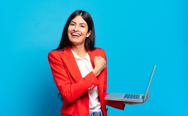 Jeune femme hispanique se sentant heureuse, positive et réussie, motivée face à un défi ou célébrant de bons résultats. concept d'ordinateur portable