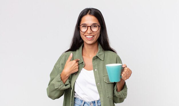 Jeune femme hispanique se sentant heureuse et se montrant elle-même avec une excitation et tenant une tasse de café