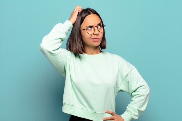 Jeune femme hispanique se sentant perplexe et confus, se grattant la tête et regardant sur le côté