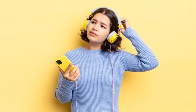 Jeune femme hispanique se sentant perplexe et confuse, se grattant la tête. casque et concept de smartphone