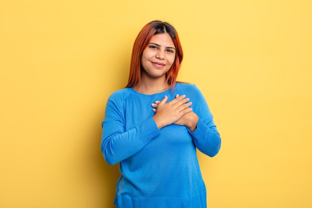 Jeune femme hispanique se sentant romantique, heureuse et amoureuse, souriant joyeusement et se tenant la main près du cœur