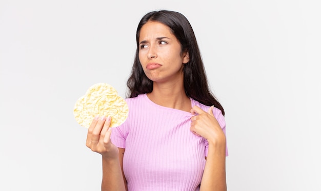 Jeune femme hispanique se sentant stressée, anxieuse, fatiguée et frustrée et tenant un biscuit au riz. concept de régime